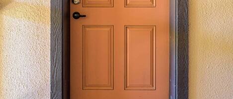 A closed wooden door with a number plate, a doorbell, and a doormat with "WELCOME" written on it.