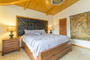 Een slaapkamer met een houten bed, twee nachtkastjes met lampen, een groot wandtapijt en een houten plafond.