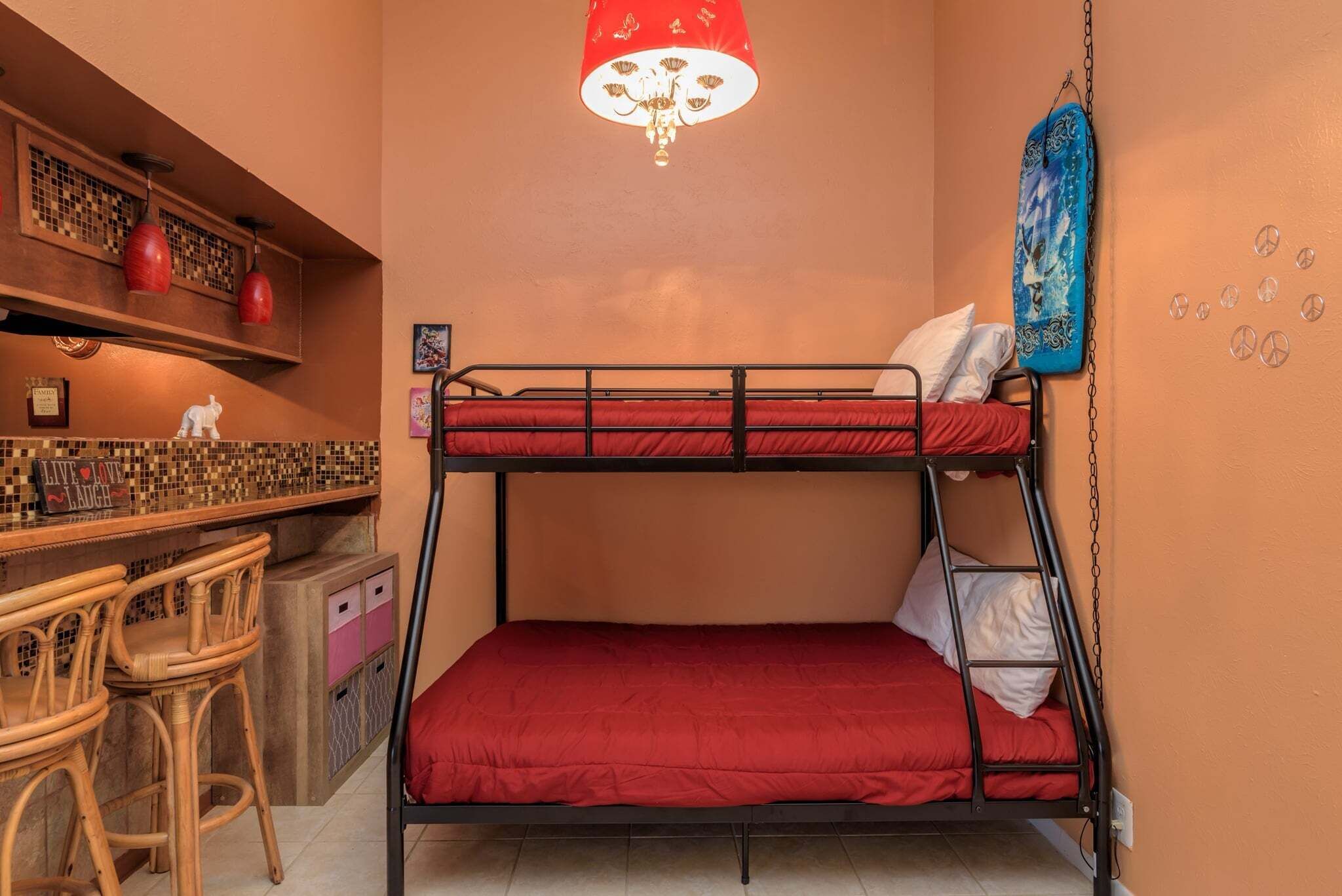 A bunk bed with a red mattress, a wooden bar with stools, and a hanging lamp.