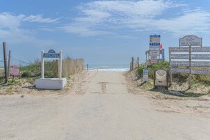 Una entrada a la playa con carteles que indican acceso a la playa, prohibido estacionar vehículos a motor y prohibido acampar durante la noche.