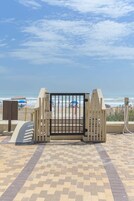 Una entrada con reja a una zona de playa, con un camino empedrado que lleva al mar.