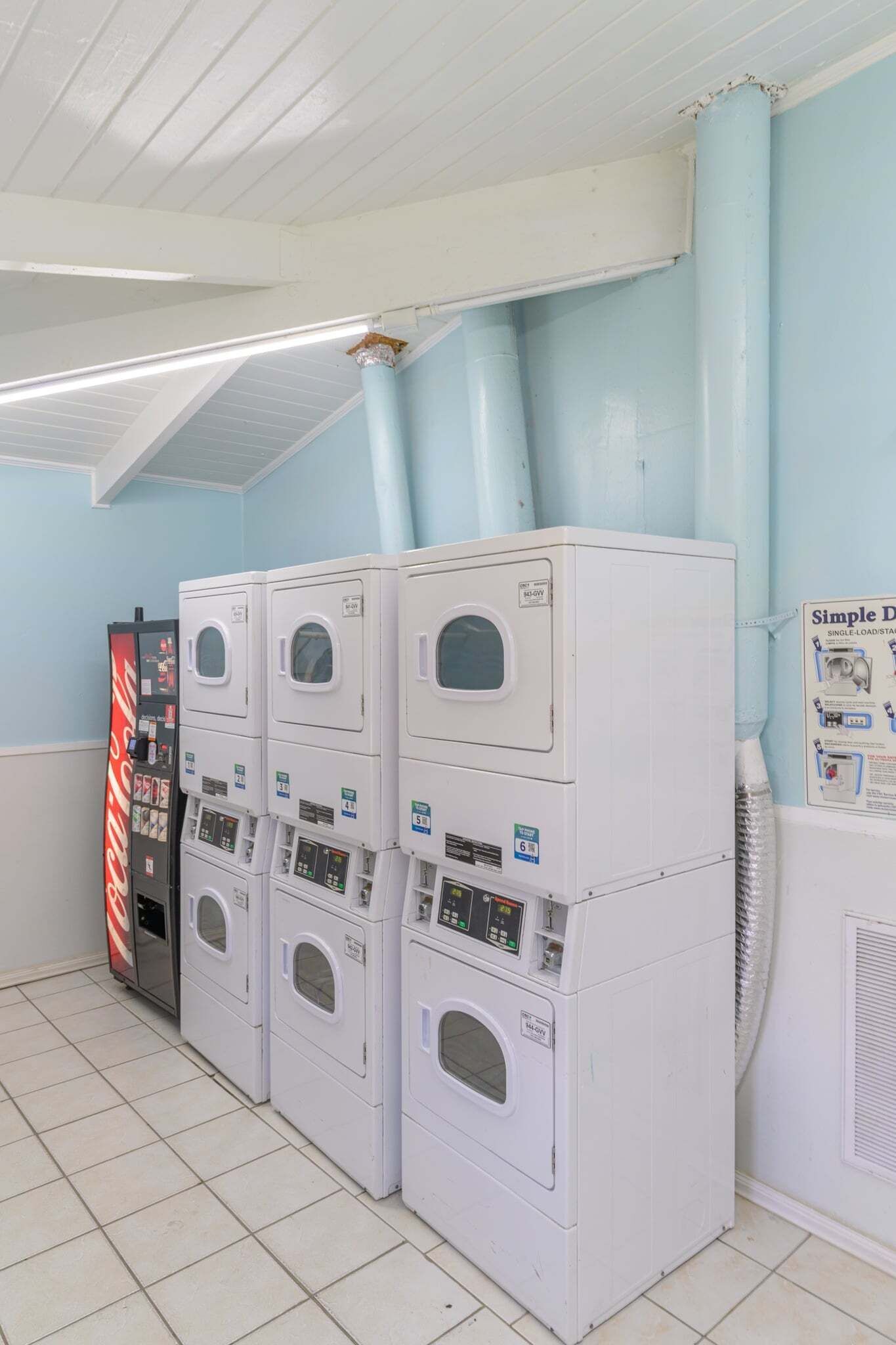 Un lavadero con varias lavadoras y secadoras apiladas, una máquina expendedora y un ventilador de techo.