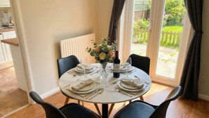 Une table ronde, dressée pour un repas à quatre, avec un vase de fleurs, une bouteille de vin et des serviettes soigneusement pliées.