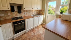 Une cuisine avec des meubles blancs, une cuisinière, un four, un évier et une fenêtre donnant sur un paysage verdoyant.