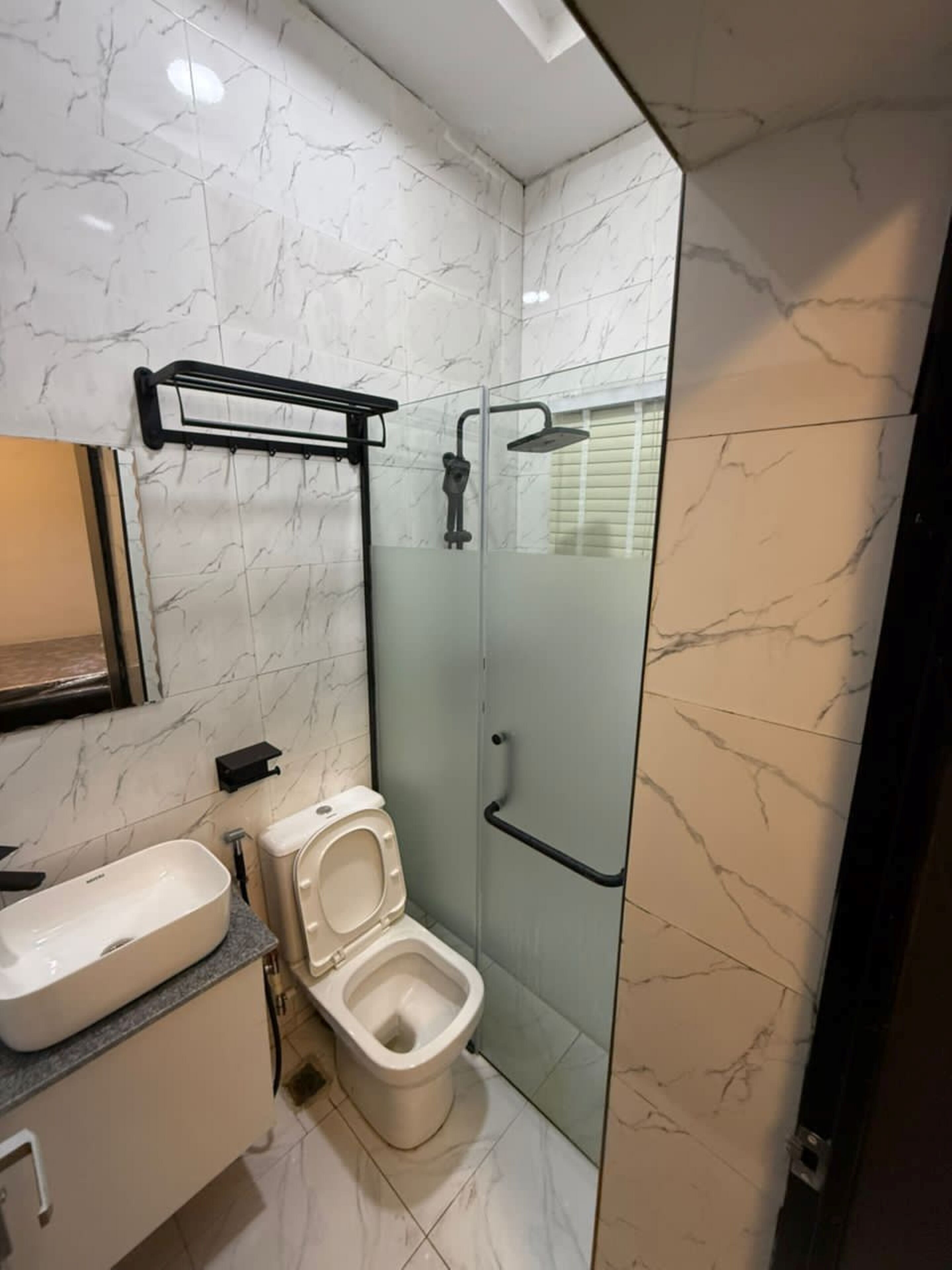 Egy modern fürőszoba, amelyben WC, mosdókagyló és zuhanyzó található.