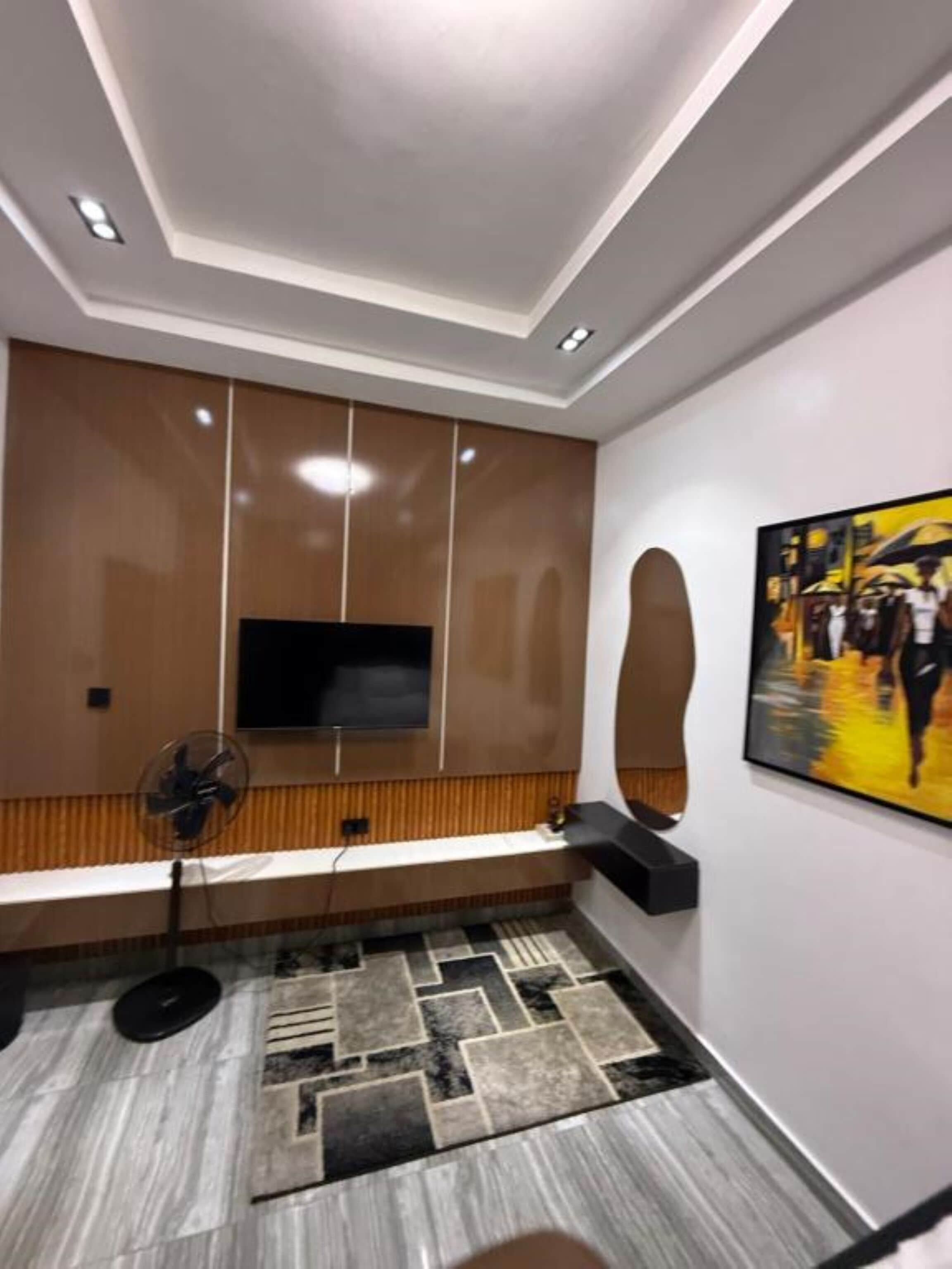 A modern living room with a built-in TV, wooden paneling, a patterned rug, and a painting on the wall.