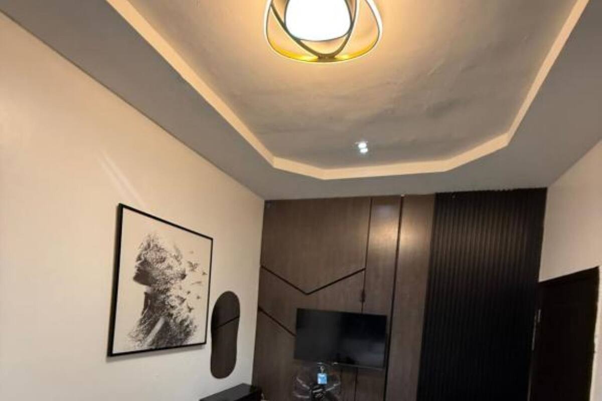 Un dormitorio moderno con una cama, un televisor montado, un ventilador de pie y un cuadro en la pared.
