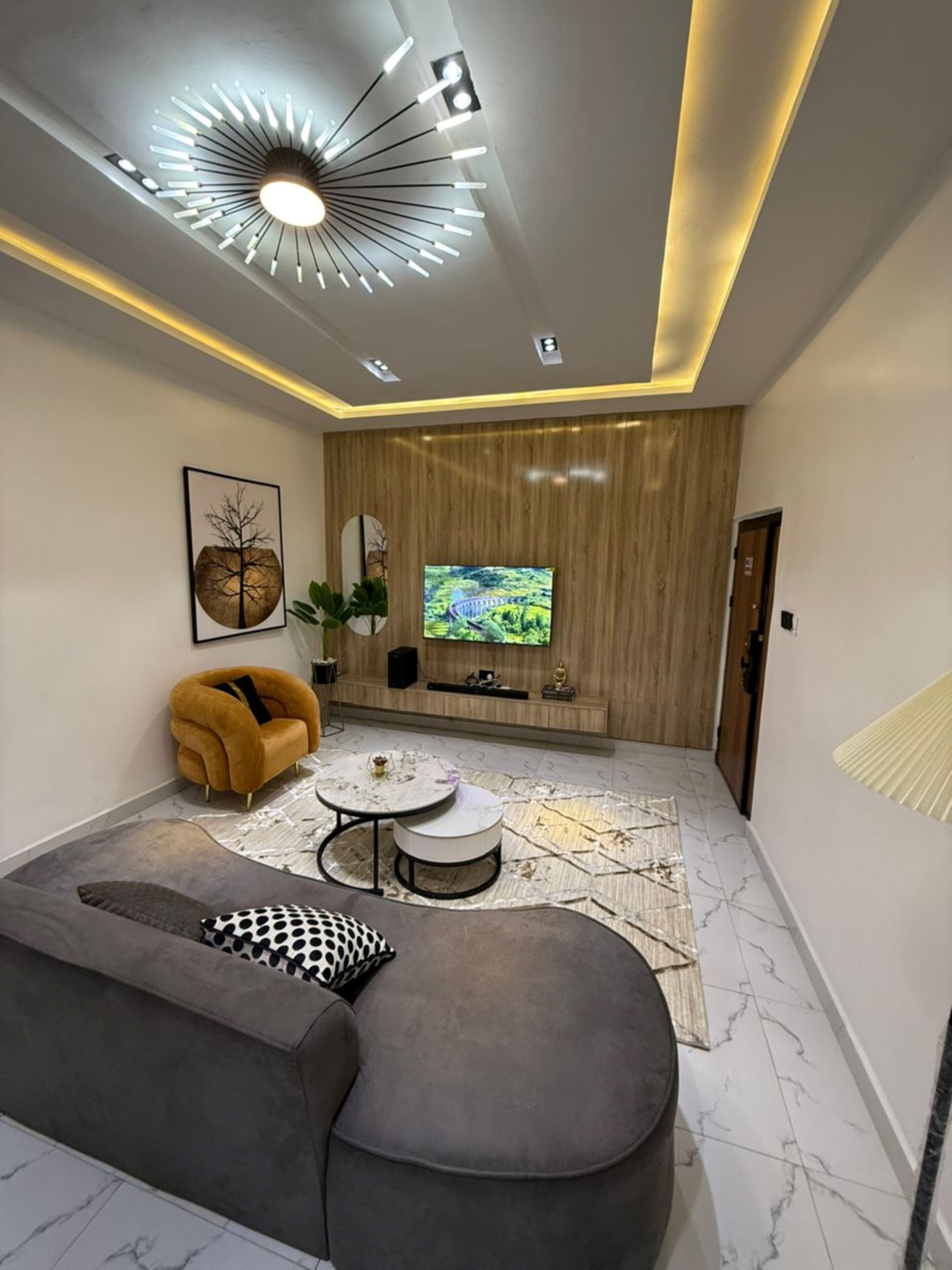 Een moderne woonkamer met een grote televisie, een bank, een bijzettafeltje en een opvallende hanglamp.