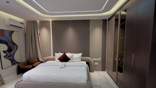 A modern bedroom with a large bed, a wardrobe, and a unique ceiling design. - Remalex Hotel and Suites (Uyo)