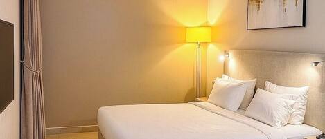 A neatly made bed with white linens, a bedside lamp, and a framed picture on the wall.