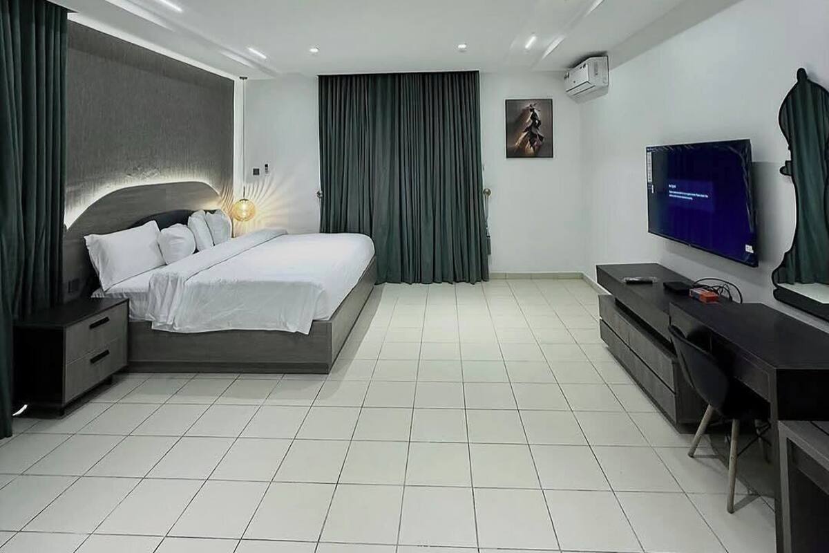 A modern bedroom with a large bed, a desk, a television, and a wall-mounted air conditioner.