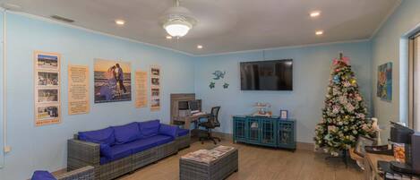 A living room with a blue sofa, a coffee table, a TV, a computer desk, and a Christmas tree.
