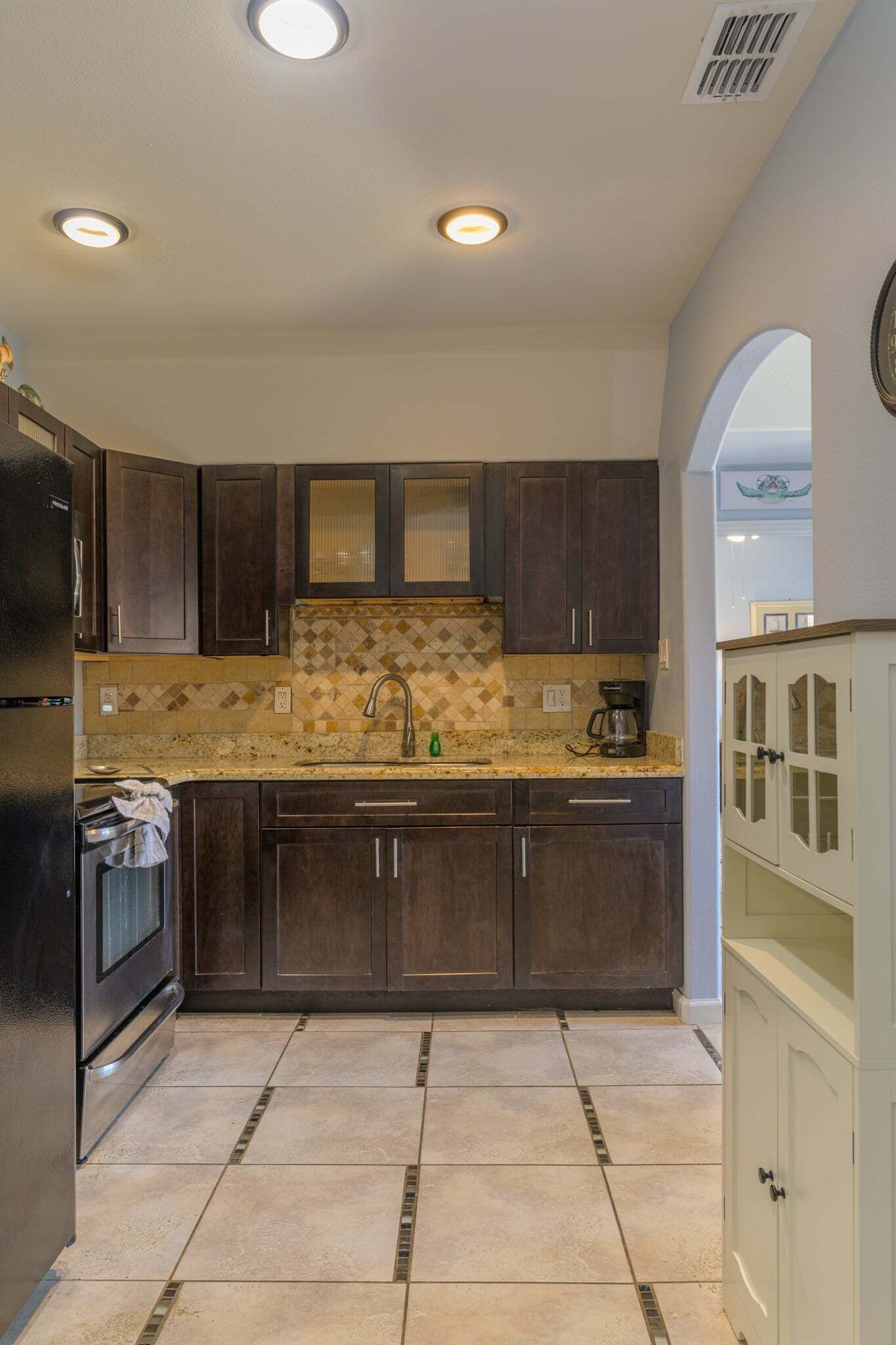 A kitchen with dark wooden cabinets, a tiled backsplash, and a granite countertop.