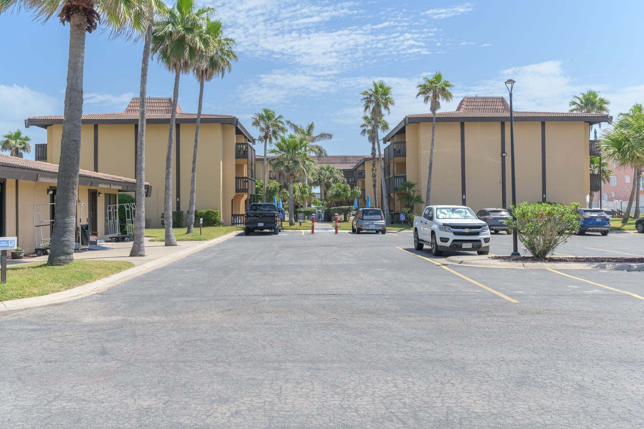 A parking lot with several cars, palm trees, and buildings with a uniform architectural style.