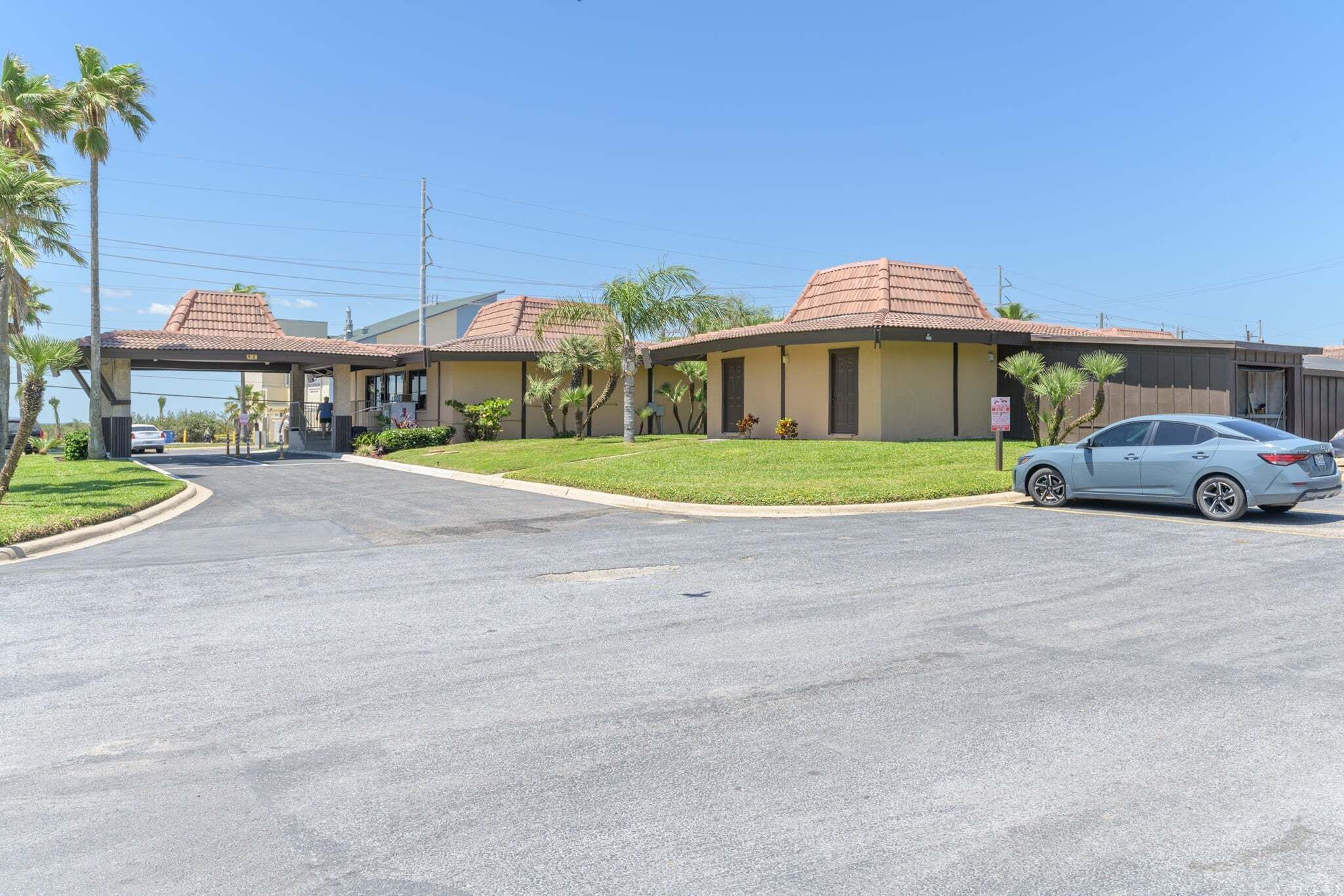 A hotel with a covered entrance, palm trees, and a car parked in front.