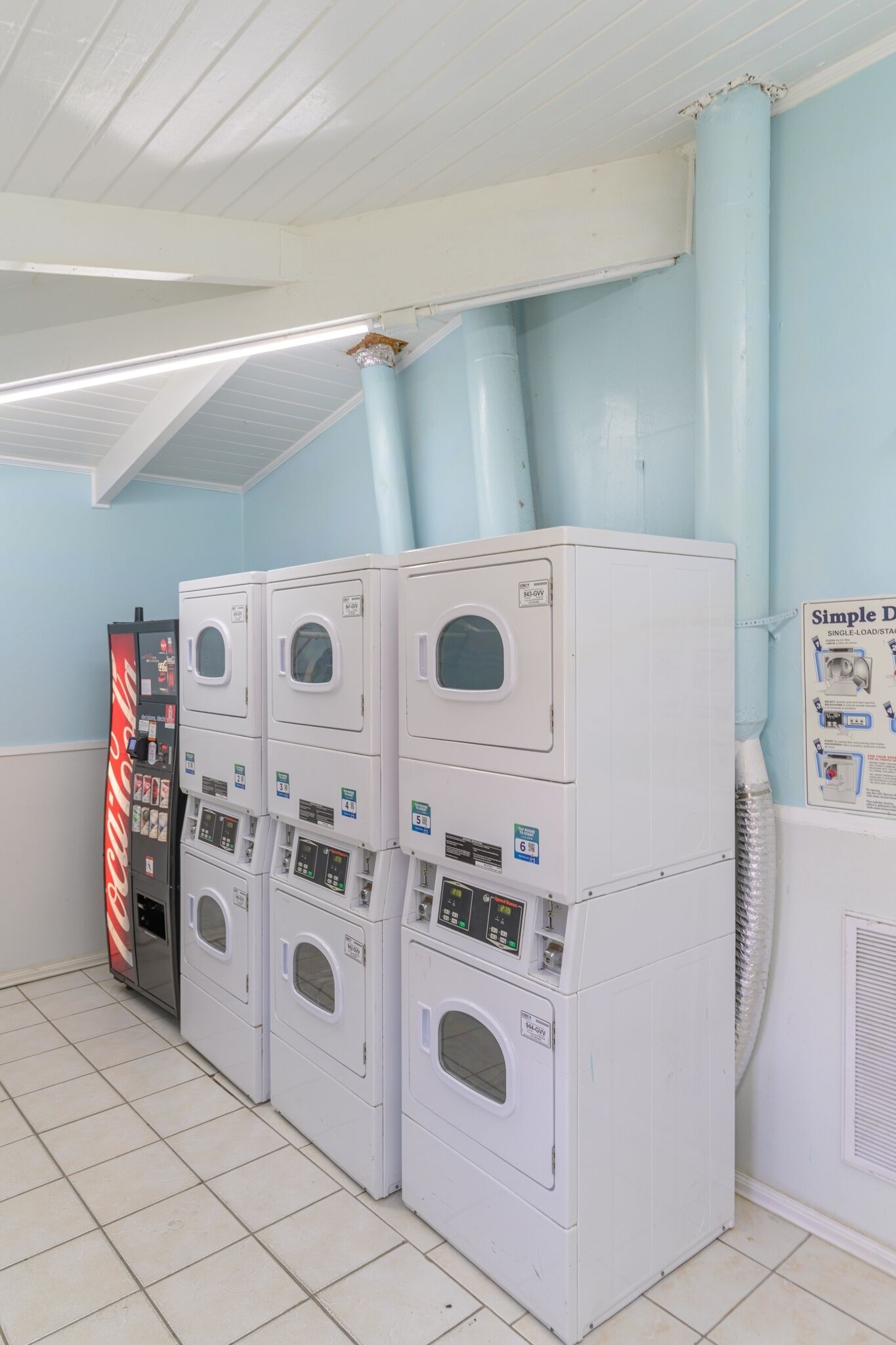 A laundry facility with multiple stacked washing machines and dryers, a vending machine, and a ceiling fan.