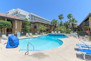 Ein Hotel mit Swimmingpool, Liegestühlen und Palmen.