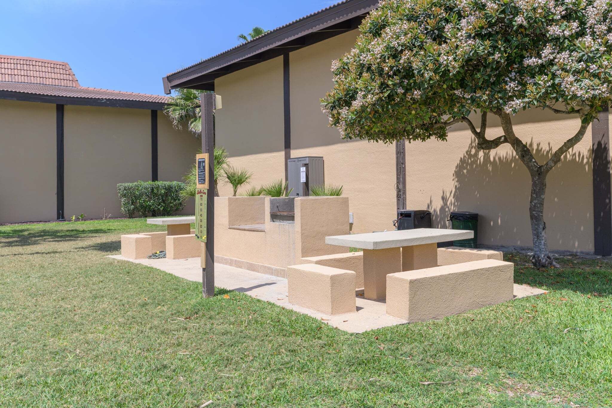 Un espace patio avec une table et des bancs, un petit arbre et un bâtiment doté d’un toit en tuiles.