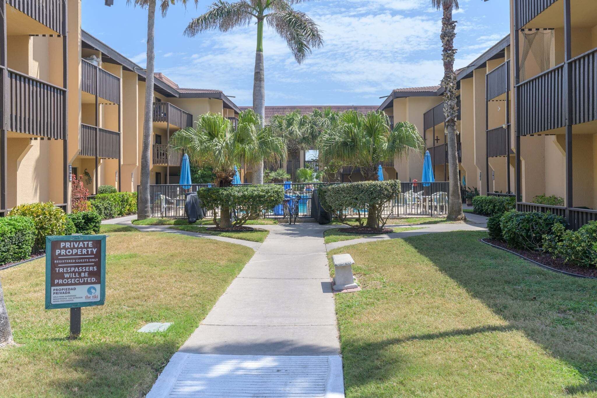 A private property with a pathway leading to a pool area, surrounded by palm trees and a well-maintained lawn.