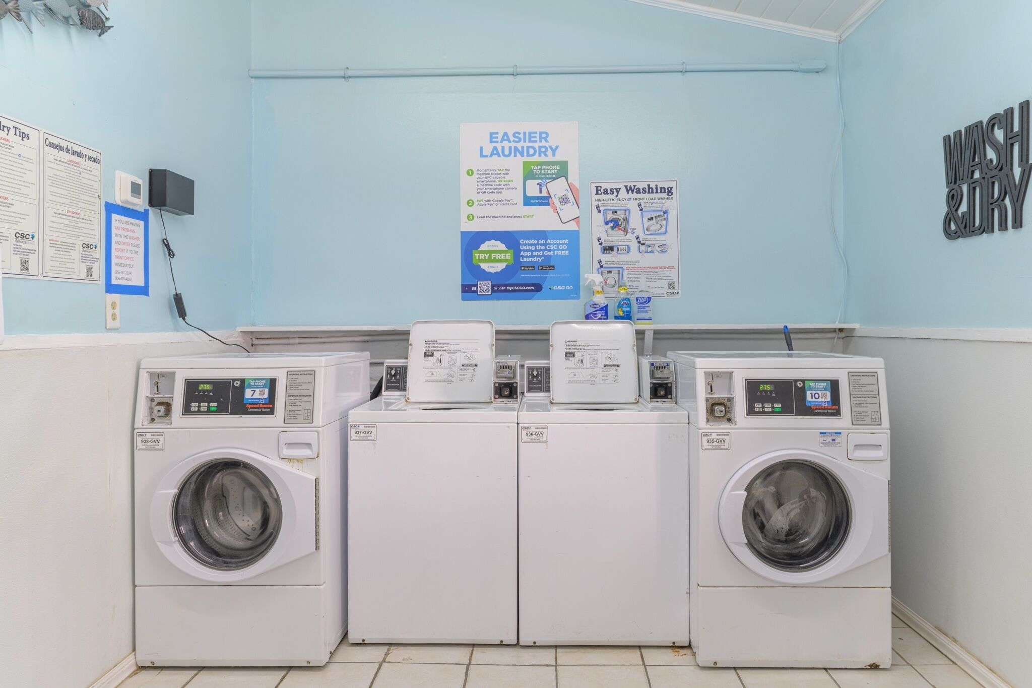 A laundry area with four washing machines, a wall-mounted phone, and informational posters.