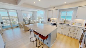 A modern kitchen with a large island, white cabinetry, and a view of the city. - Shoreline Towers 3101 3 Bedroom Condo (Destin)