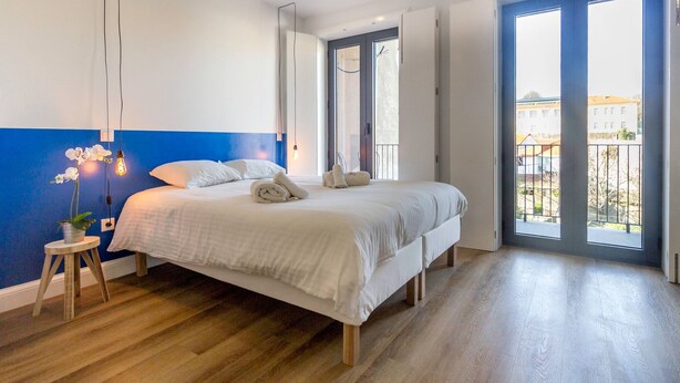 Una camera da letto moderna con un letto grande, un comodino con una pianta e vista all'esterno tramite una porta scorrevole.