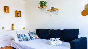 Een netjes opgemaakt slaapkamer met een bed, kussens, een kleine plant en een wandplank met bloemen.
