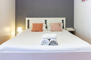 A neatly made bed with white linens and two pillows, a bedside table with a lamp, and a wall-mounted light fixture. - Guest H4U - Porto City Center (Porto)
