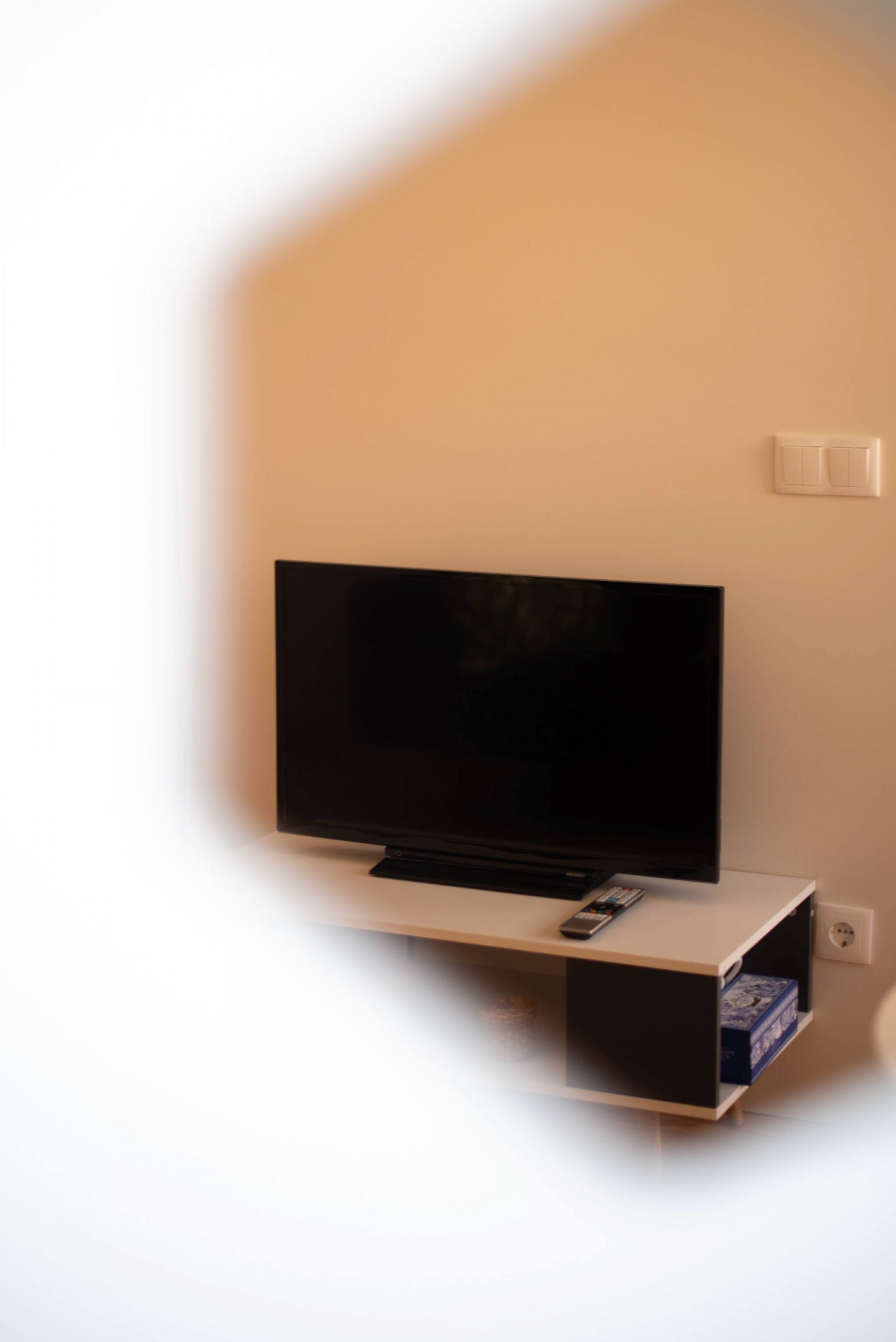 A flat-screen TV mounted on a wall with a remote control on a stand below it.