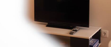 A flat-screen TV mounted on a wall with a remote control on a stand below it.