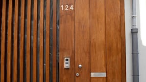 Een houten poort met het nummer 124, een metalen intercom en een betegelde muur erboven.