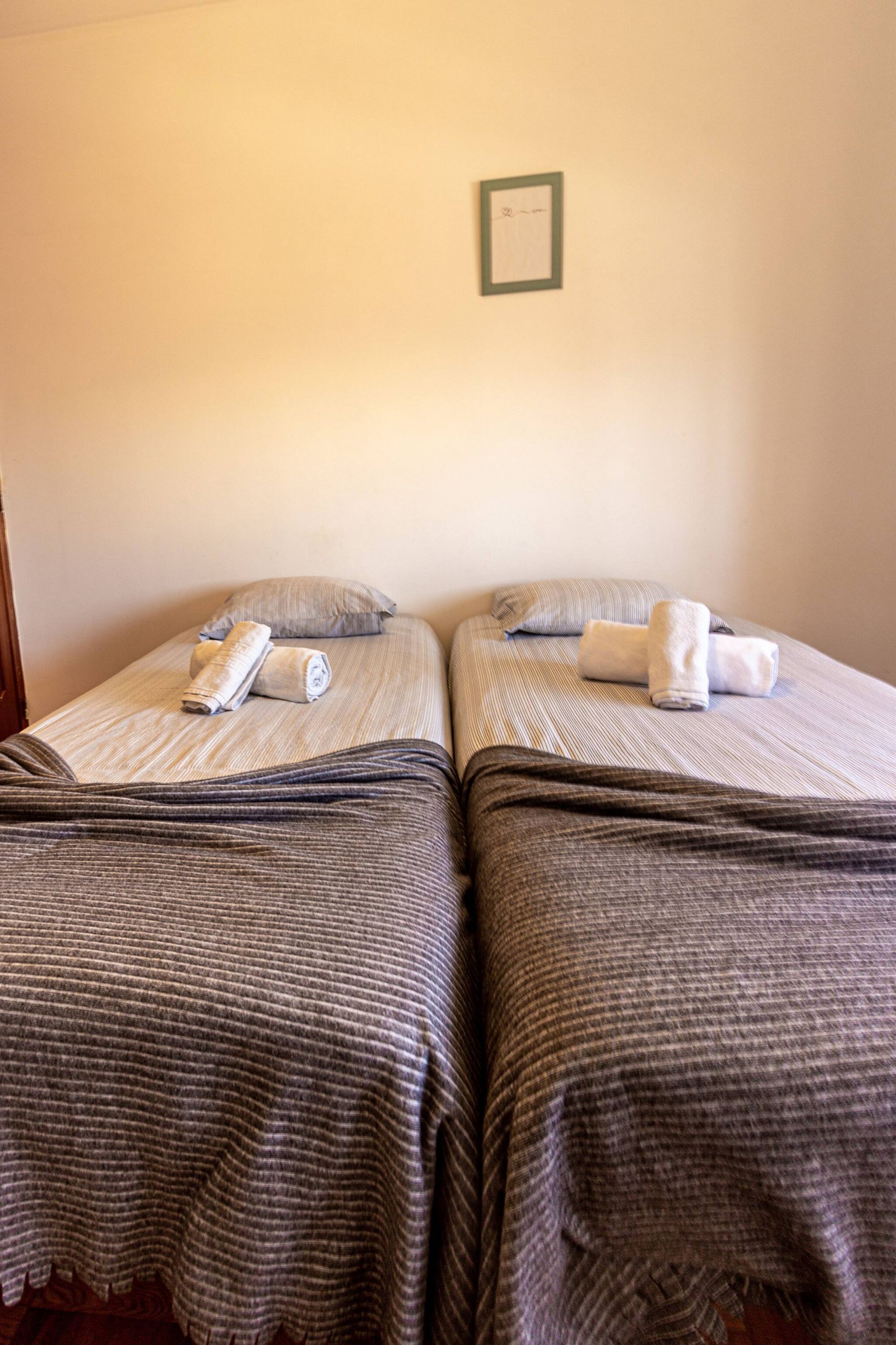 Two twin beds with striped bedding and rolled towels, a framed picture on the wall, and a wooden door on the left.