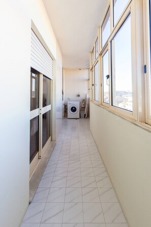 Un couloir étroit avec un lave-linge et un étendoir, de grandes fenêtres et un sol carrelé.