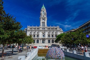 A historic building with a prominent clock tower, a central fountain, and a plaza with seating and trees. - Guest H4U - Porto Ribeira View Mercadores (Porto)