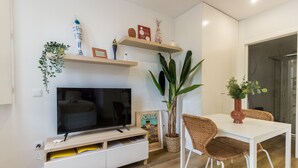 A modern living room with a flat-screen TV, a dining table, wicker chairs, and decorative shelves. - Guest H4U - Heroismo 2F (Porto)