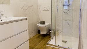 A modern bathroom with a glass shower enclosure, a white vanity, and a marble-tiled wall. - Guest H4U - Heroismo 2F (Porto)