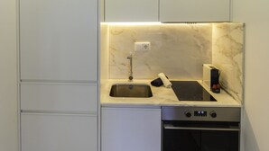 A compact kitchen with white cabinets, a built-in oven, and a sink with a marble countertop. - Guest H4U - Heroismo 2F (Porto)