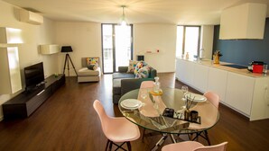 A modern living room with a glass dining table, pink chairs, a sofa, and a TV. - Guest H4U - Bonjardim Pop Art (Porto)