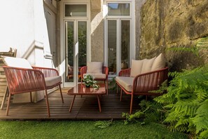 An outdoor patio with wicker furniture, a wooden table, and a glass door leading to a garden. - Guest H4U - Bonjardim Garden City Center (Porto)
