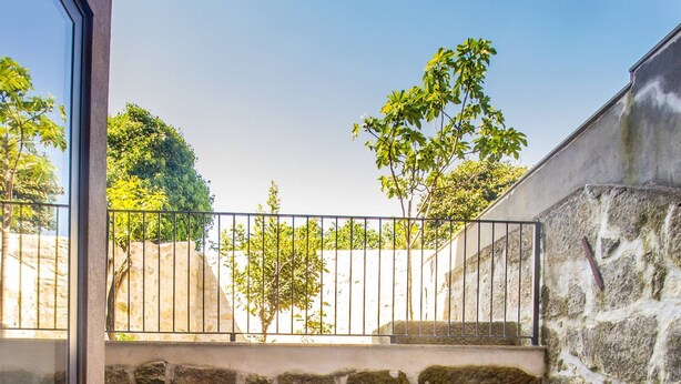 A patio area with a stone wall, a wooden bench, and a cushioned seating area. - Guest H4U - Hero smo Terrace Ground Floor (Porto)