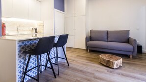 A modern kitchen with a marble countertop and two bar stools. There is a grey sofa and a wooden stool in the living area. - Guest H4U - Hero smo Terrace Ground Floor (Porto)