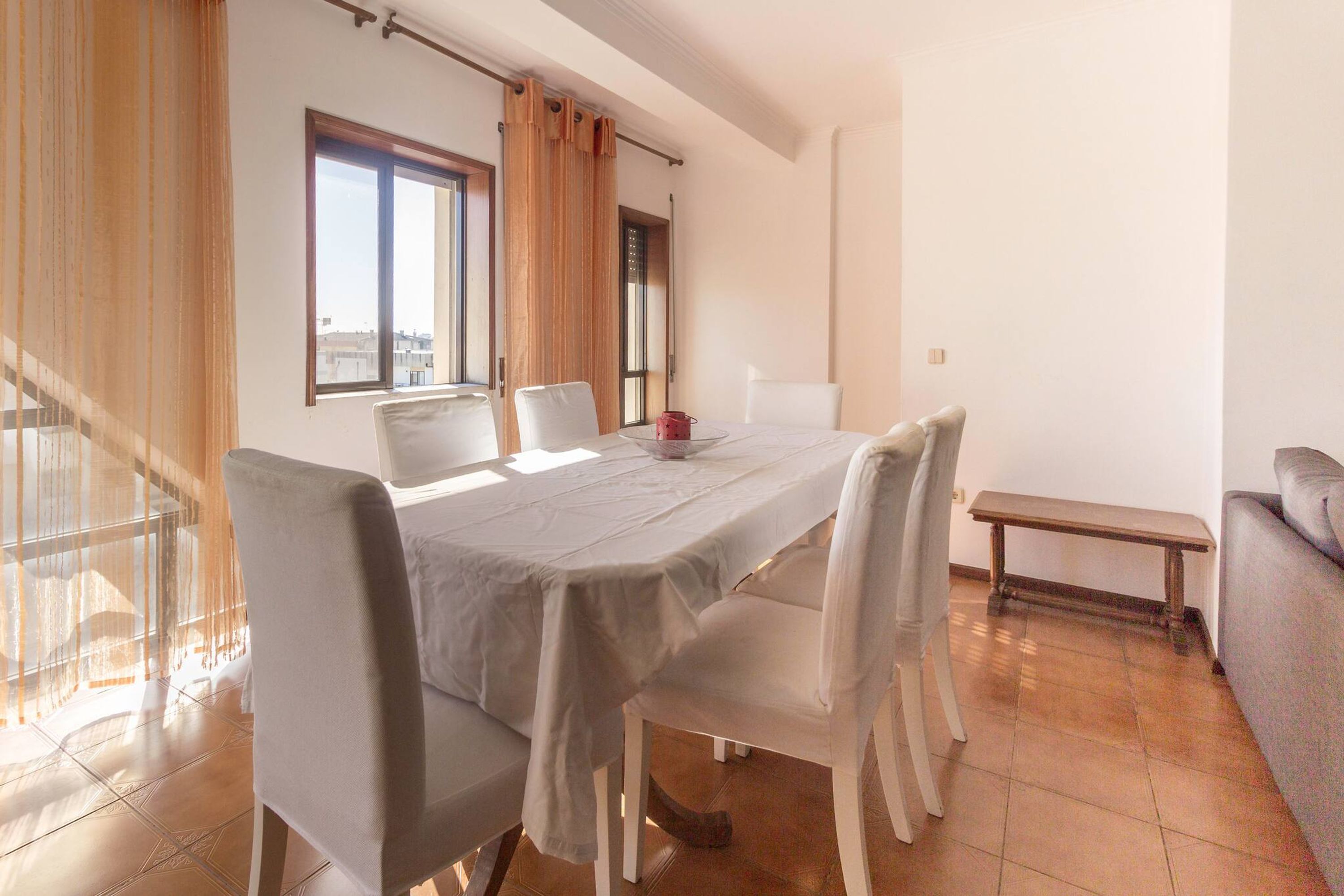 Un espace repas comprenant une table, des chaises, un banc et offrant une vue sur la ville grâce à de grandes fenêtres.