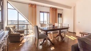 A spacious living area with a large dining table, multiple chairs, and a sofa. There are large windows providing a view of the outside. - Guest House 4U - Povoa Seaside (Povoa De Varzim)