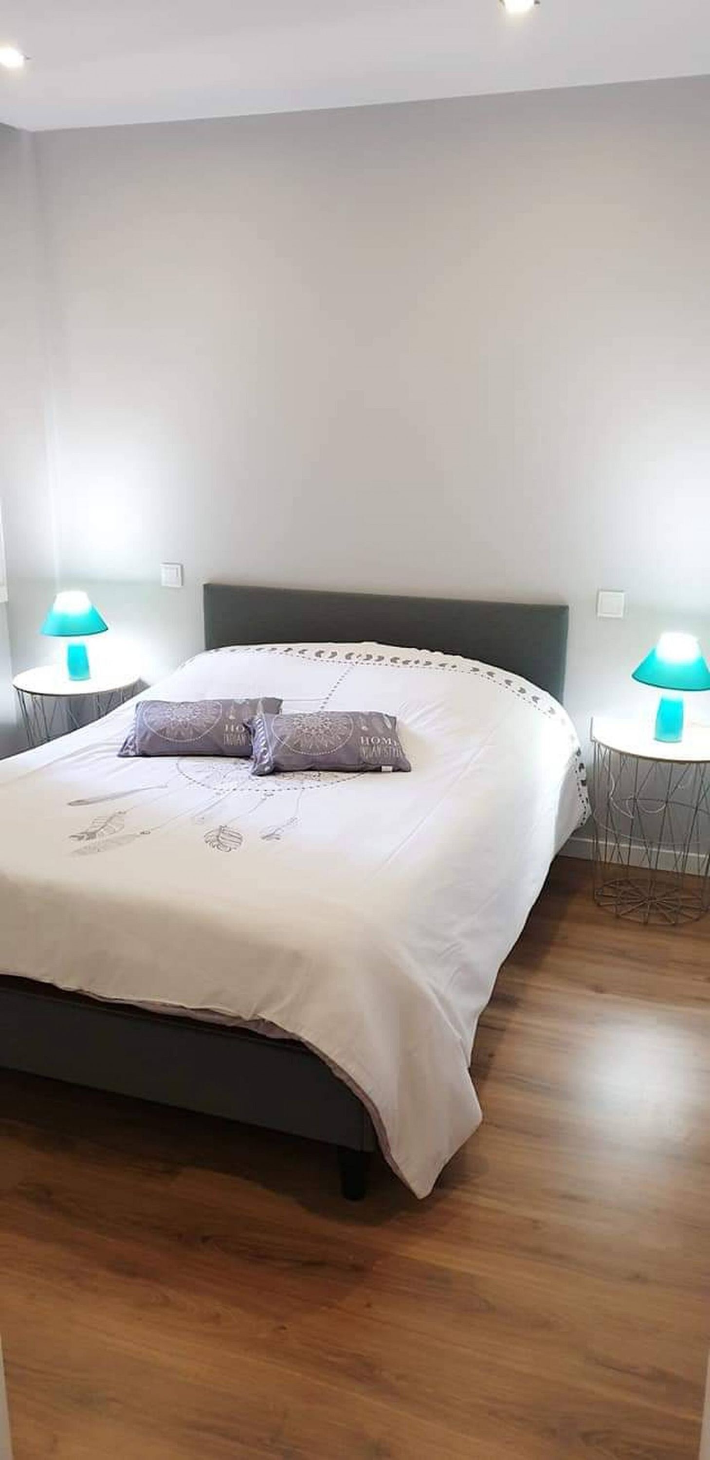 A neatly made bed with a white bedspread and two pillows, flanked by two bedside tables with lamps.