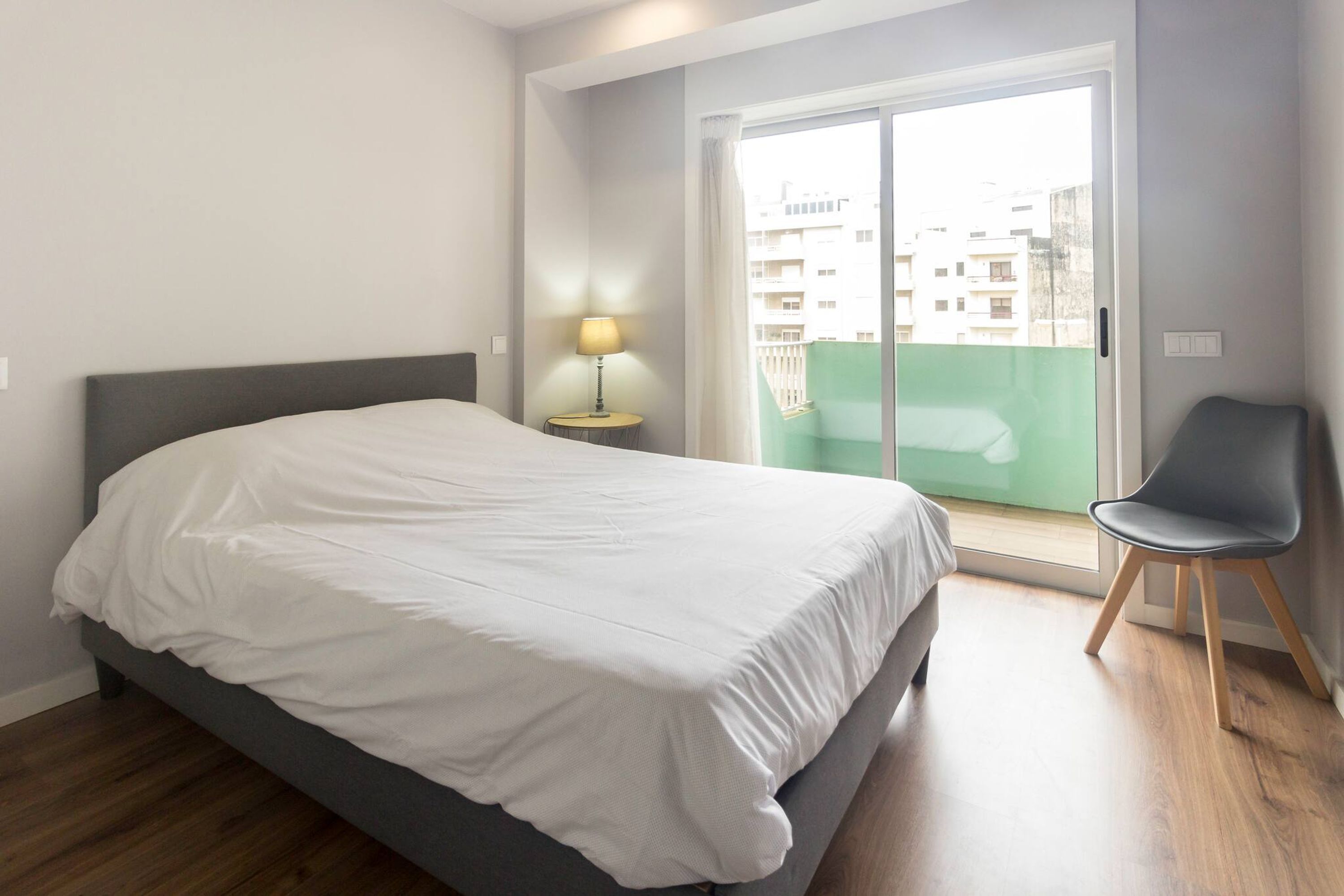 Une chambre à coucher comprenant un lit, une table de chevet avec une lampe, une chaise et une porte-fenêtre coulissante donnant sur un balcon.