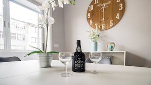 A table with a bottle of Porto Reccia Tawny wine, two wine glasses, a potted orchid, and a wooden wall clock.