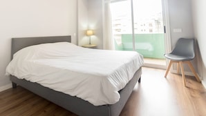 A bedroom with a bed, a nightstand with a lamp, a chair, and a sliding glass door to a balcony.