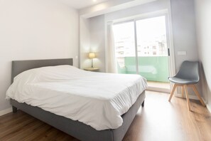 A bedroom with a bed, a nightstand with a lamp, a chair, and a sliding glass door to a balcony. - Guest H4U - P voa Summer (Povoa De Varzim)