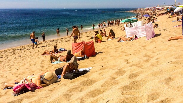 A crowded beach with people sunbathing and walking along the shore.