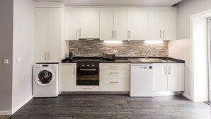 A modern kitchen with white cabinets, a built-in oven, a dishwasher, and a washing machine.